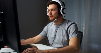 Mann sitzt vor PC mit Headset und spielt augenscheinlich ein Computerspiel
