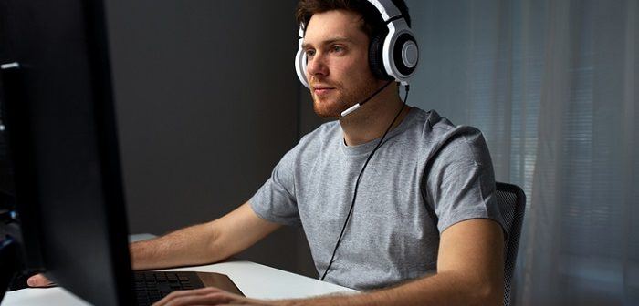 Mann sitzt vor PC mit Headset und spielt augenscheinlich ein Computerspiel