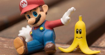 Mario sitzt mit einer Banane mit Gesicht auf einem Holzuntergrund